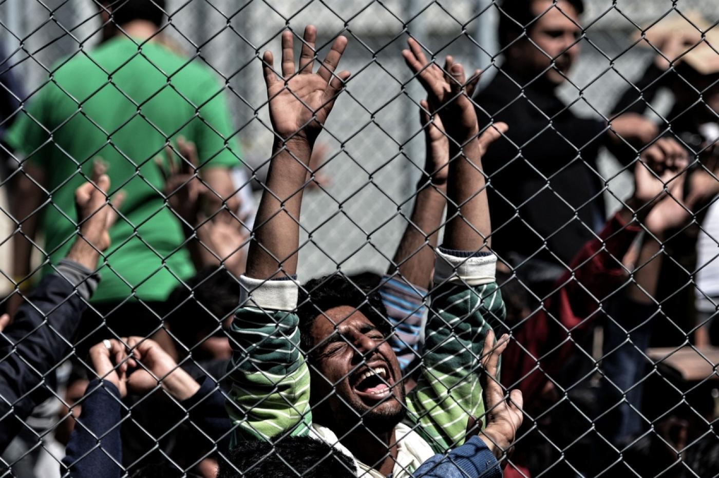 A man holds his hands up behind a chain link fence as migrants protest inside the Moria detention center on Lesbos on April 5 2016 AFP
